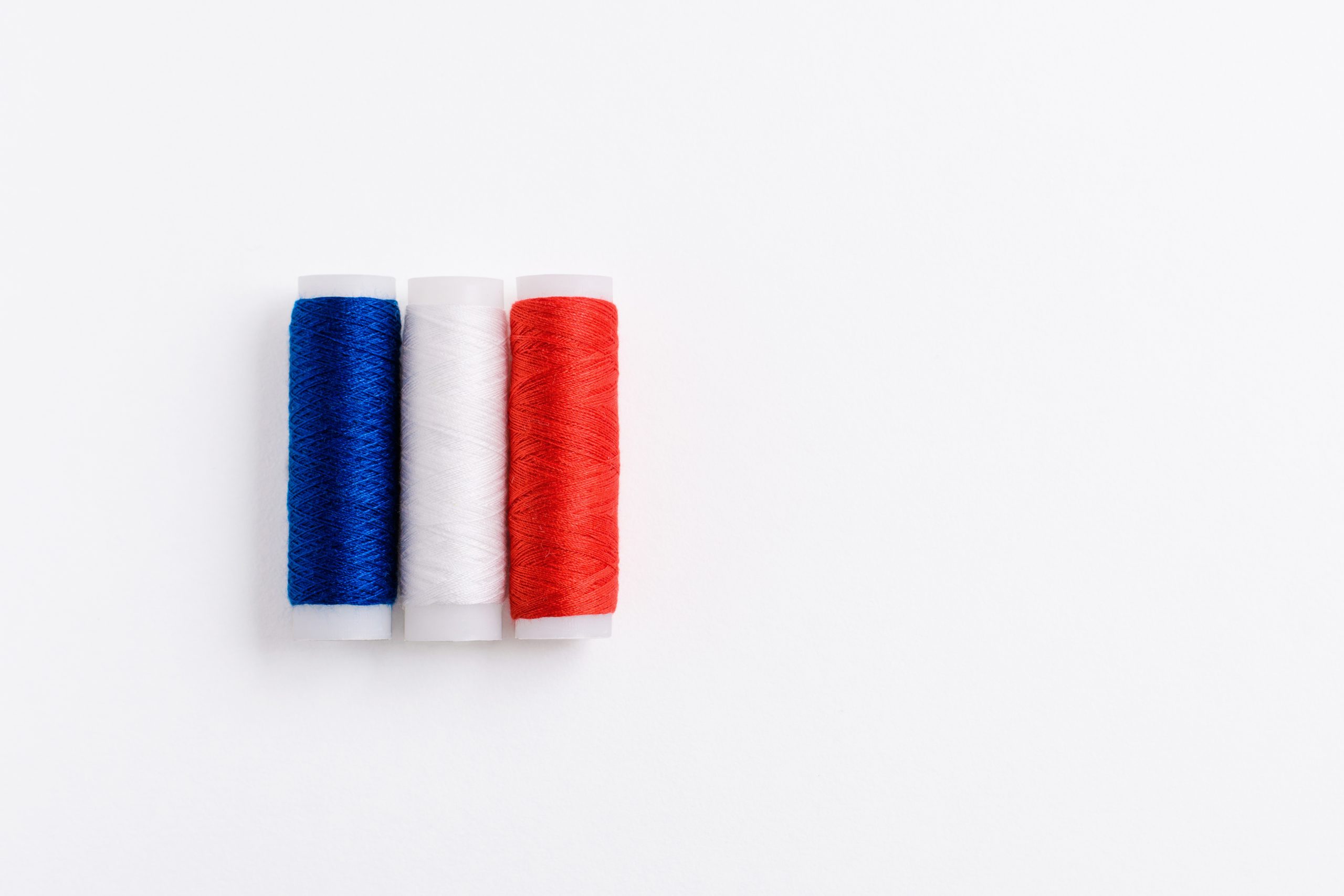 Three spools of thread for sewing are stacked in the form of the flag of France on a white background. Concept of French patriotism and the country's garment industry. There is a free empty space.Three spools of thread for sewing are stacked in the form of the flag of France on a white background. Concept of French patriotism and the country's garment industry. There is a free empty space.